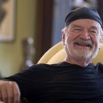 Sculptor David Hostetler smiling in a black cap, seated at home on Nantucket
