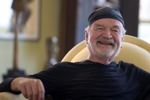 Sculptor David Hostetler smiling in a black cap, seated at home on Nantucket