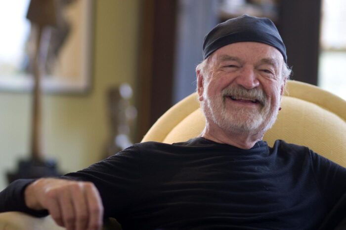 Sculptor David Hostetler smiling in a black cap, seated at home on Nantucket